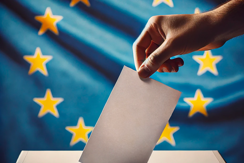 Une main déposant un bulletin de vote dans un ballot. Derrière un drapeau Européen 